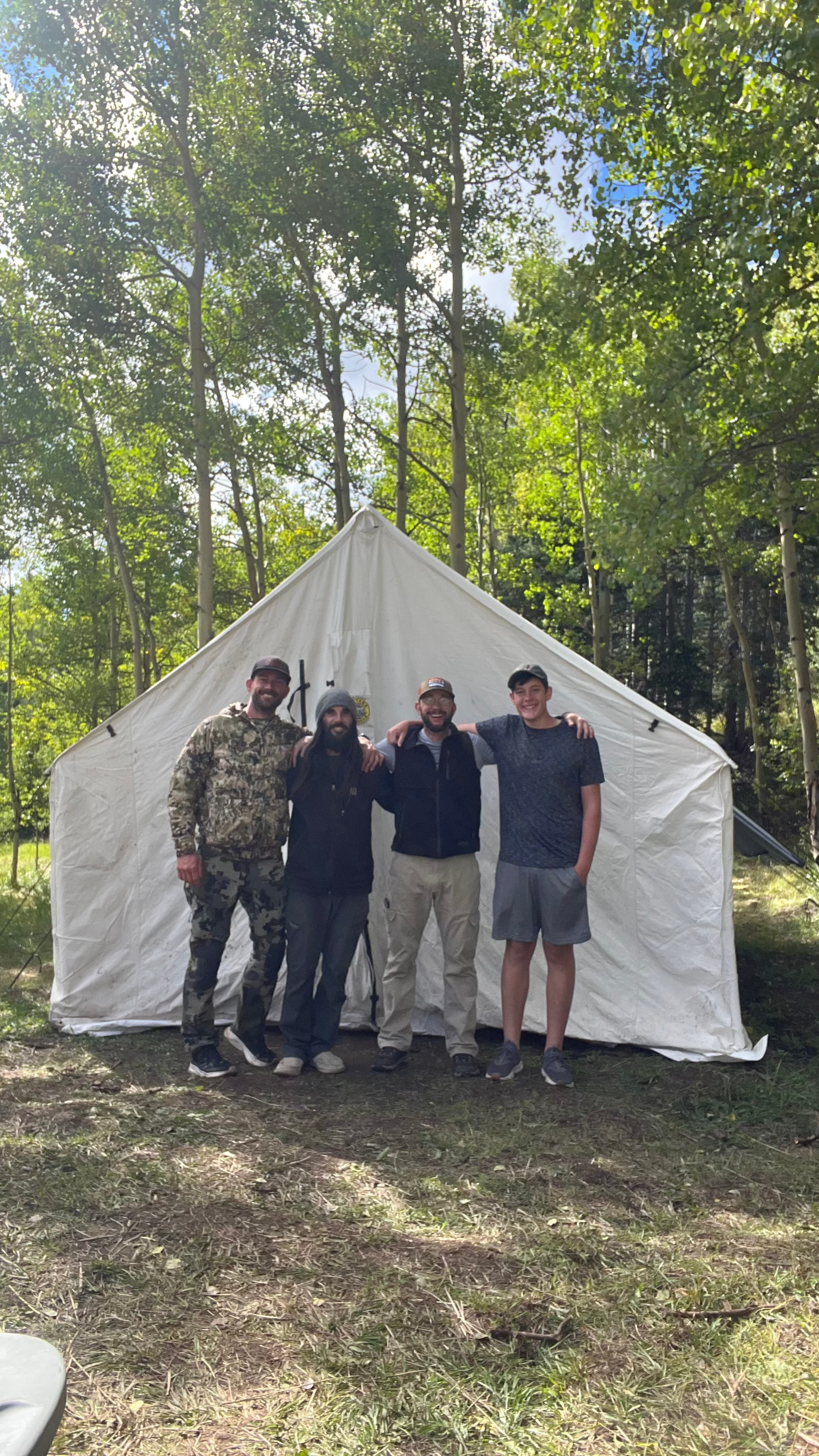 Four men arm-in-arm in front of a wall tent in the aspens