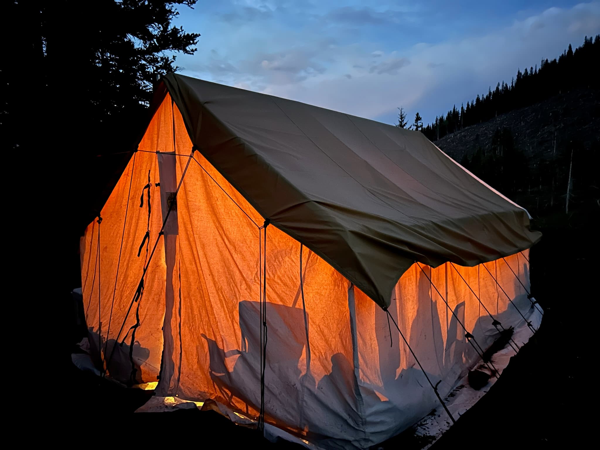 Wall tent glowing at dusk with silhouettes inside