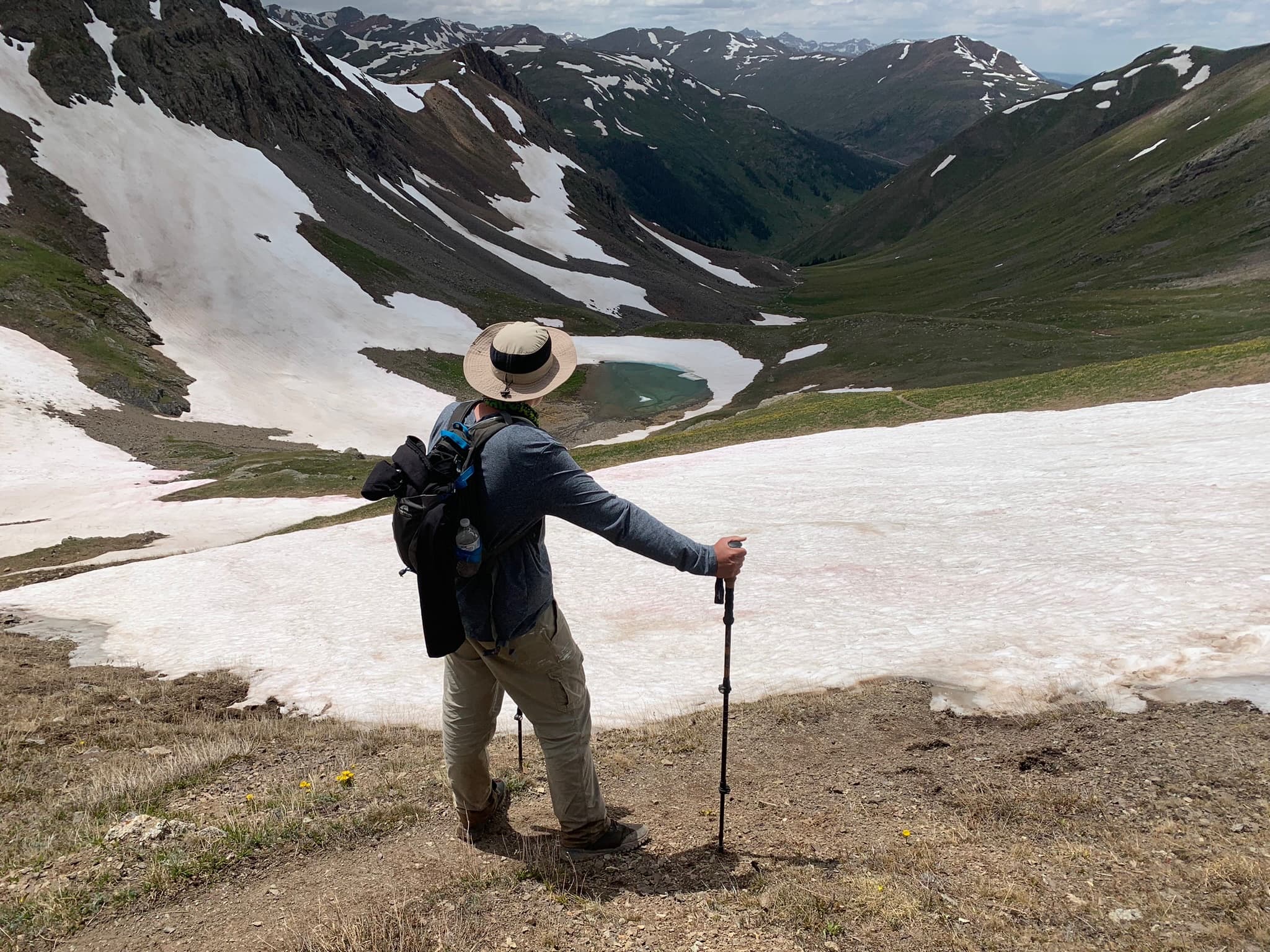 Hiker overlooking an alpine lake from a snowfield rim