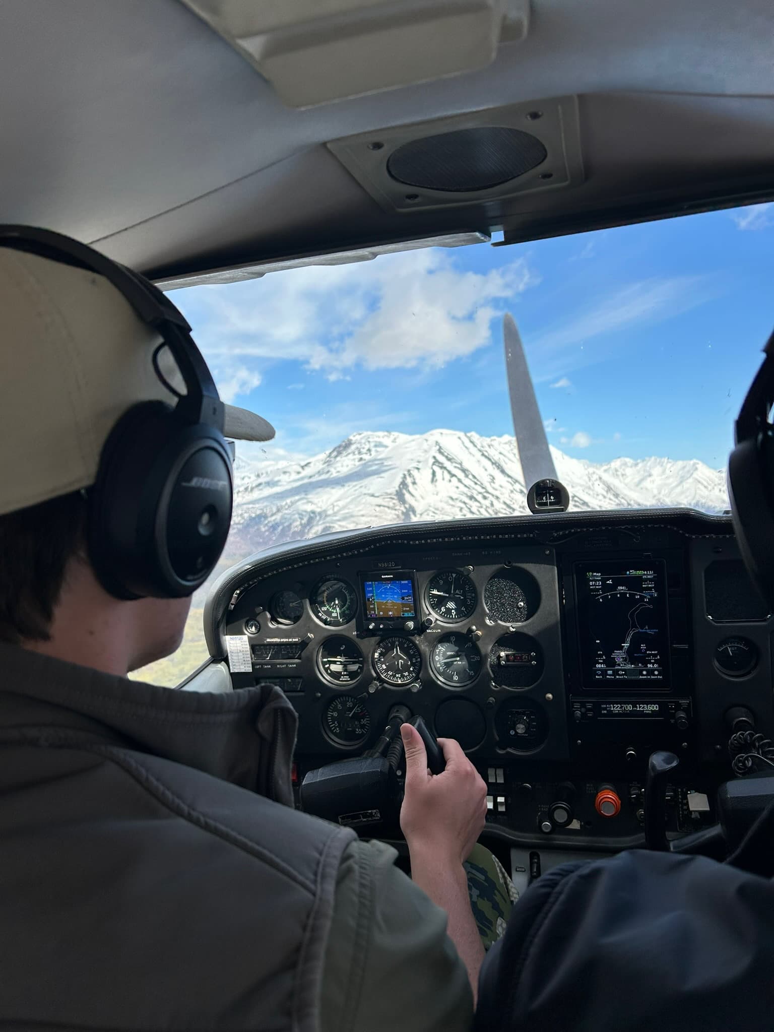 Pilot in headset flying a small plane toward snow peaks
