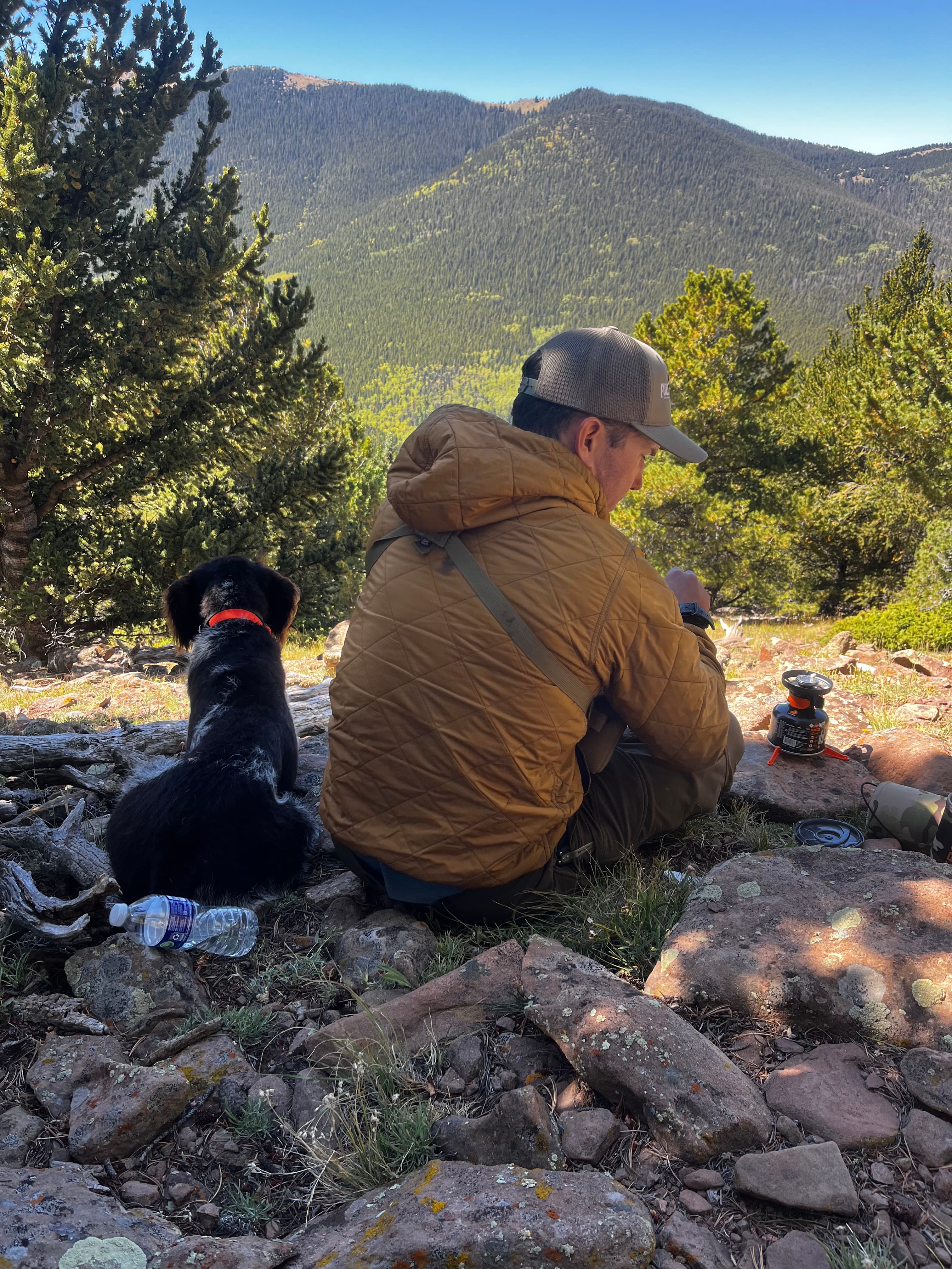 Man with a black dog on a rocky ridge, glassing the valley