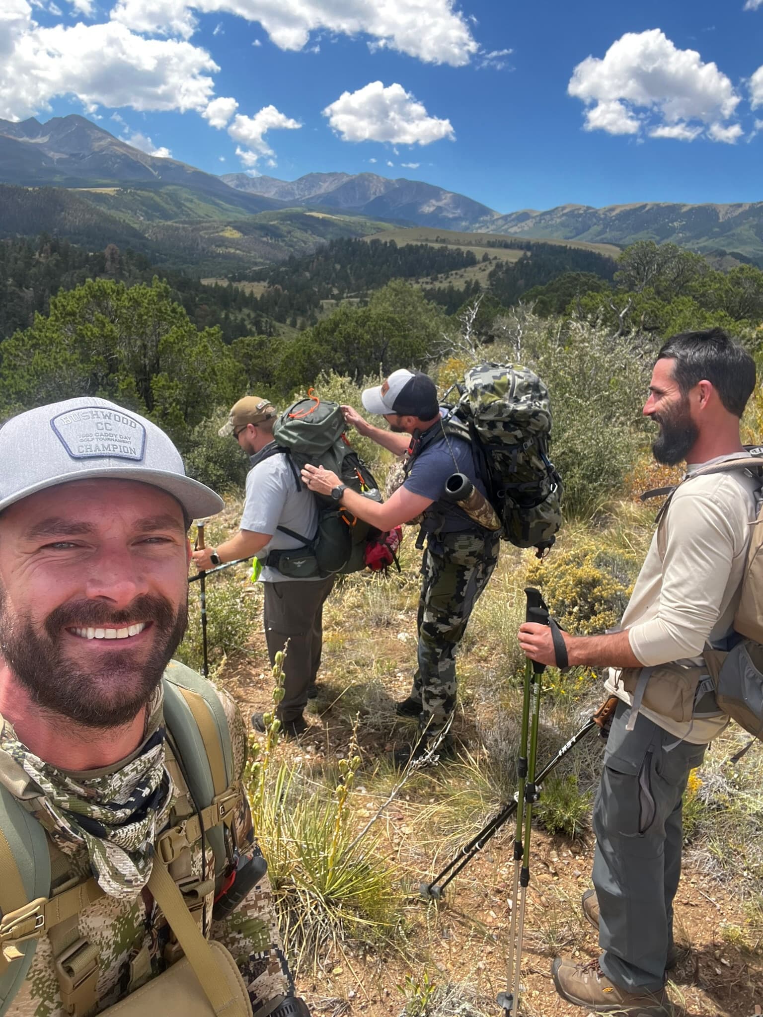Three backpackers loading packs on an alpine ridge