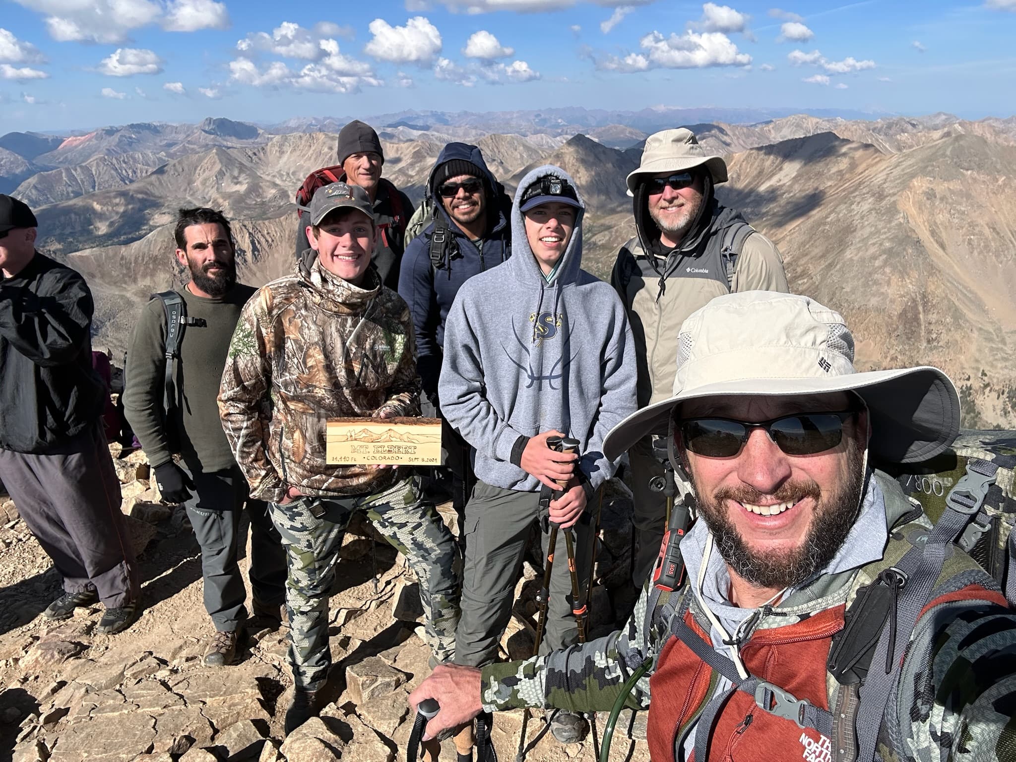 Summit group photo with the summit register and a big mountain range