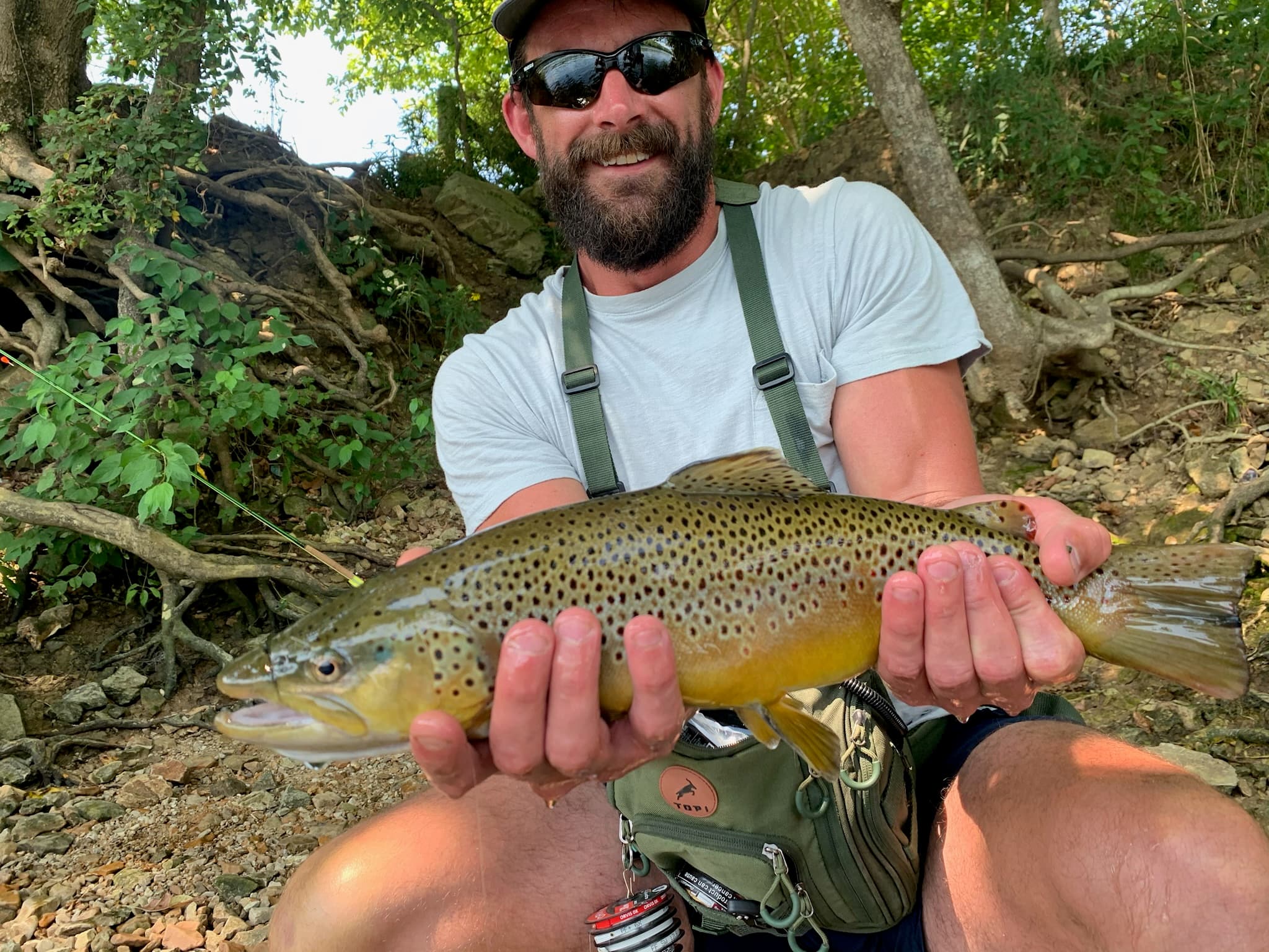 Brown trout held by a fly angler, vest detail