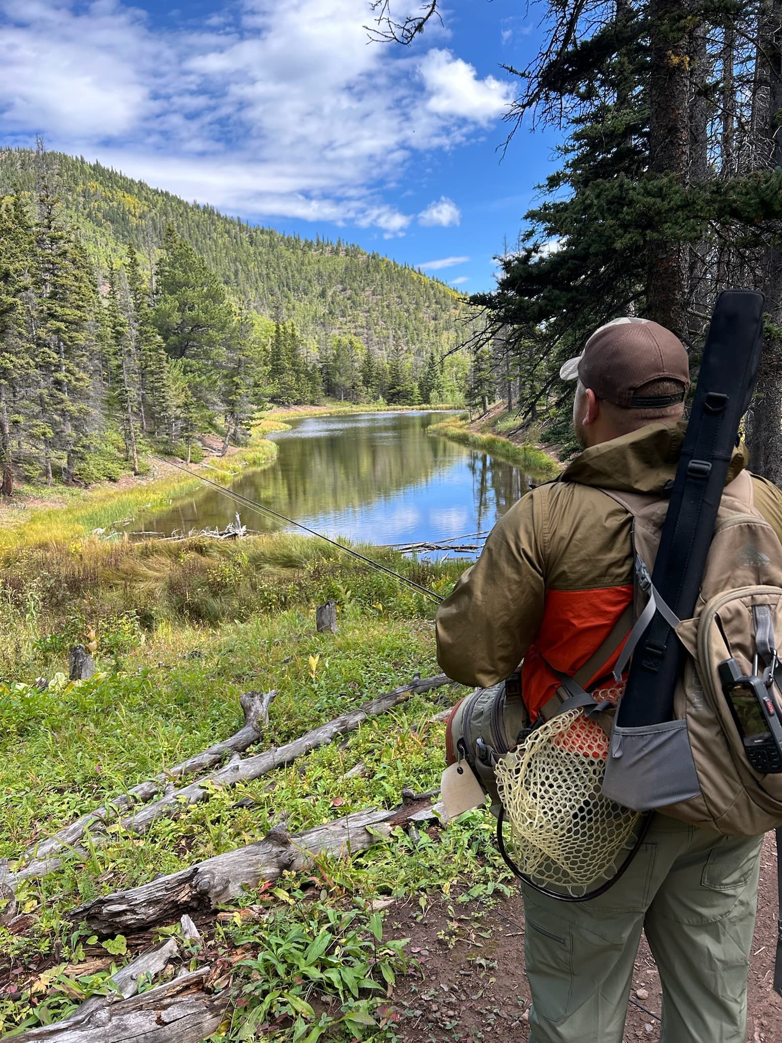 Angler with a fly rod and net watching a beaver pond in fall colors
