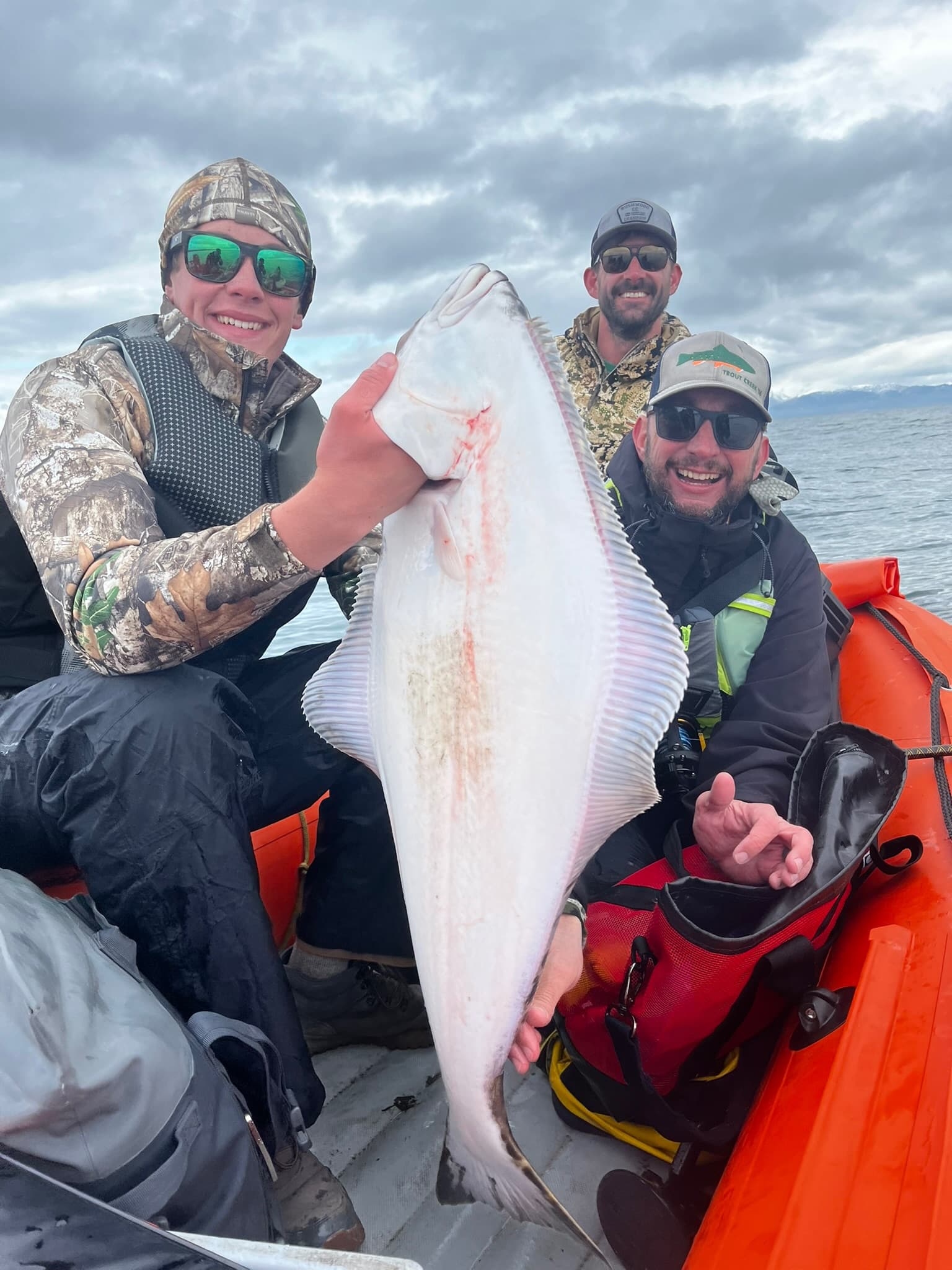 Three men on an orange zodiac with a huge halibut