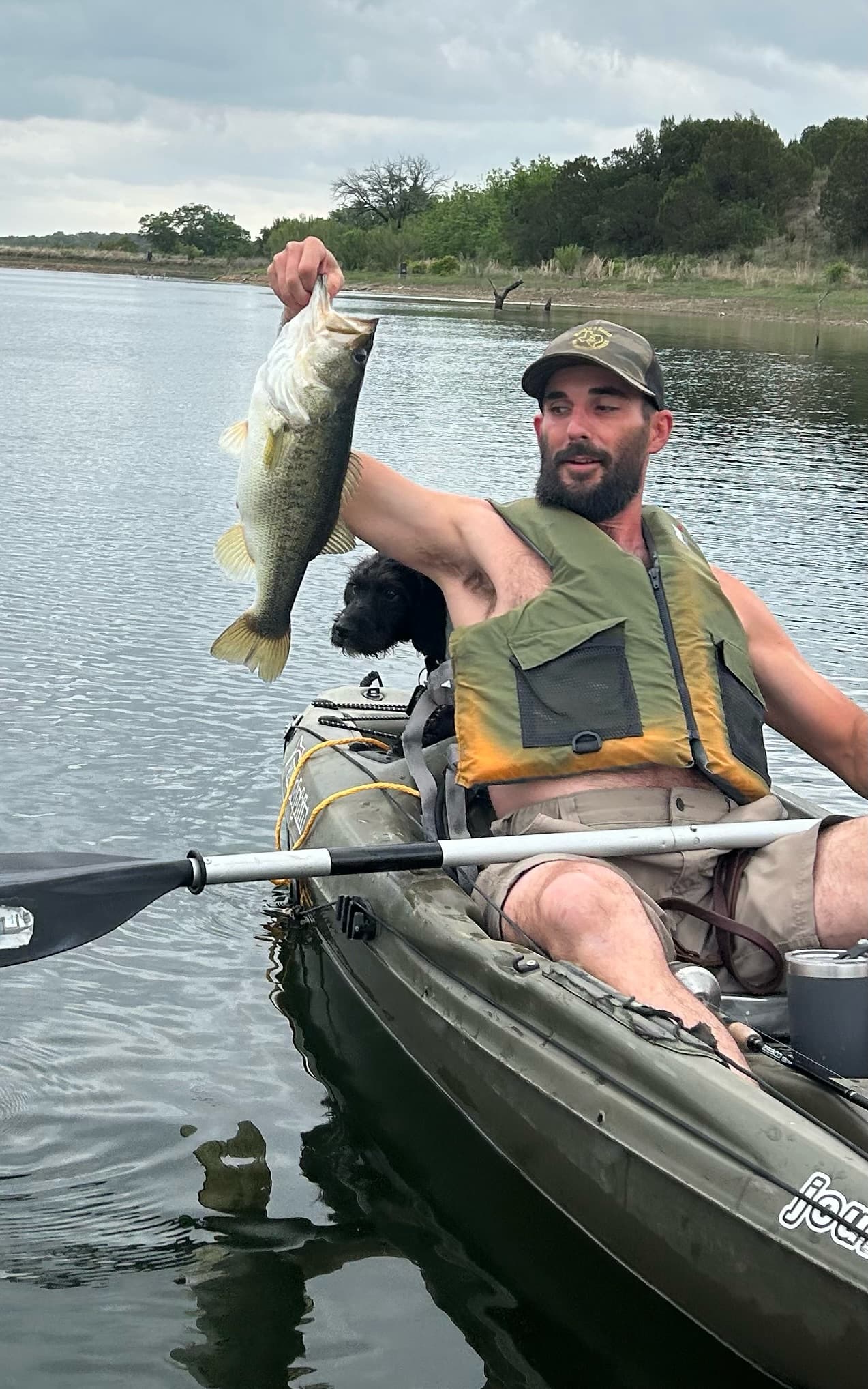 Kayak angler holding a bass with a black dog co-pilot