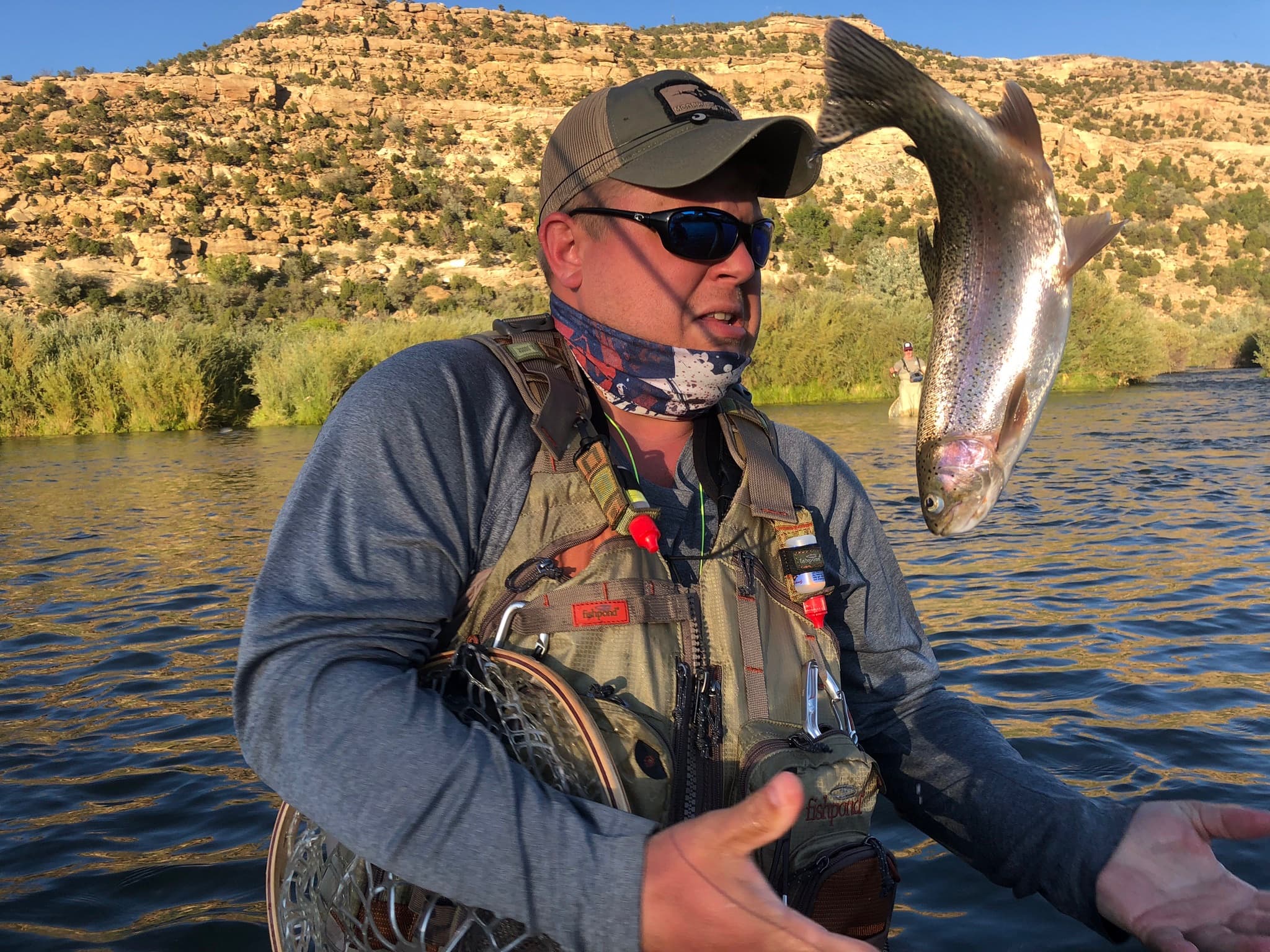 Fly angler with a rainbow trout on a raft, red cliffs