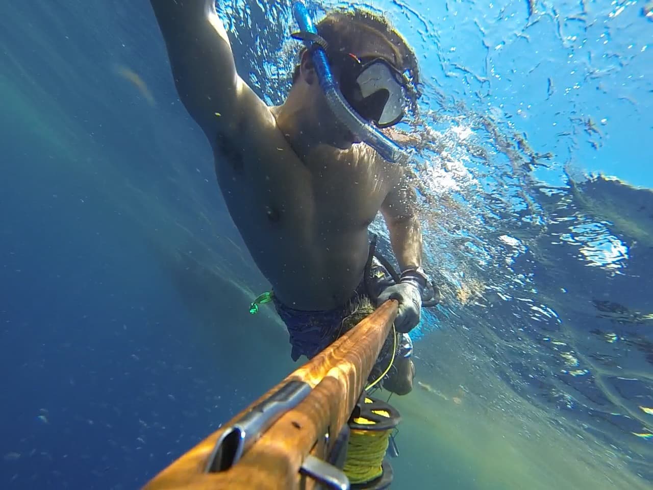 Underwater spearfisher with a loaded gun, sunlight rays through water