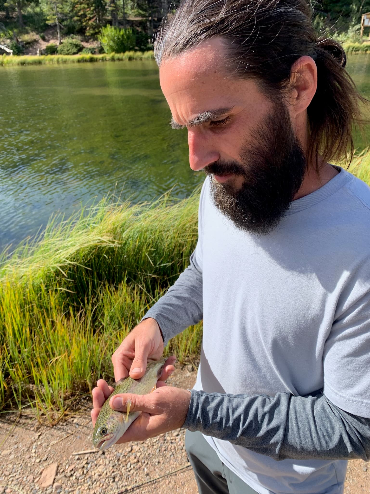 Angler kneeling for a gentle trout release near a grass bank