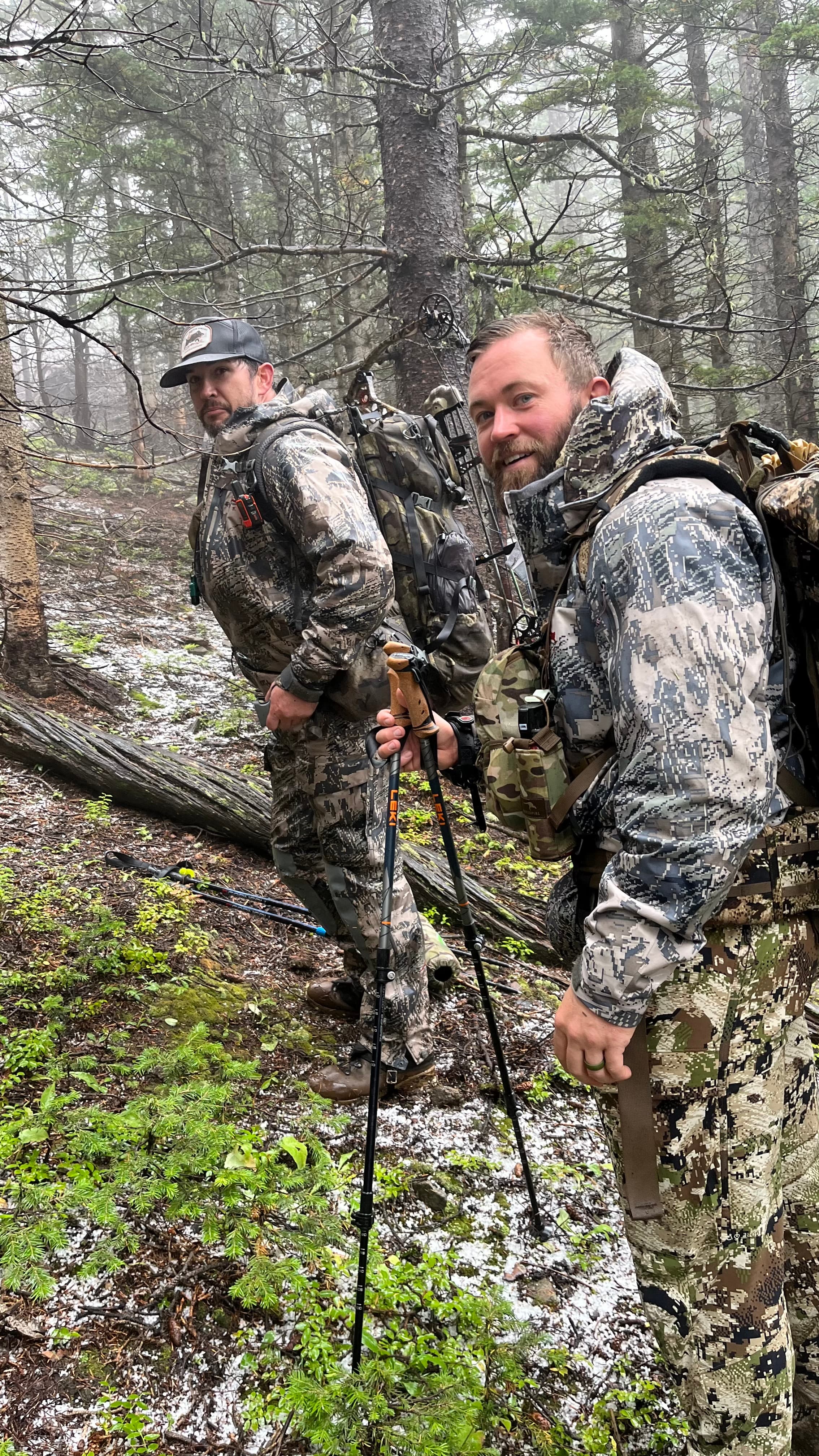 Two men in camo with backpacks hiking through misty timber