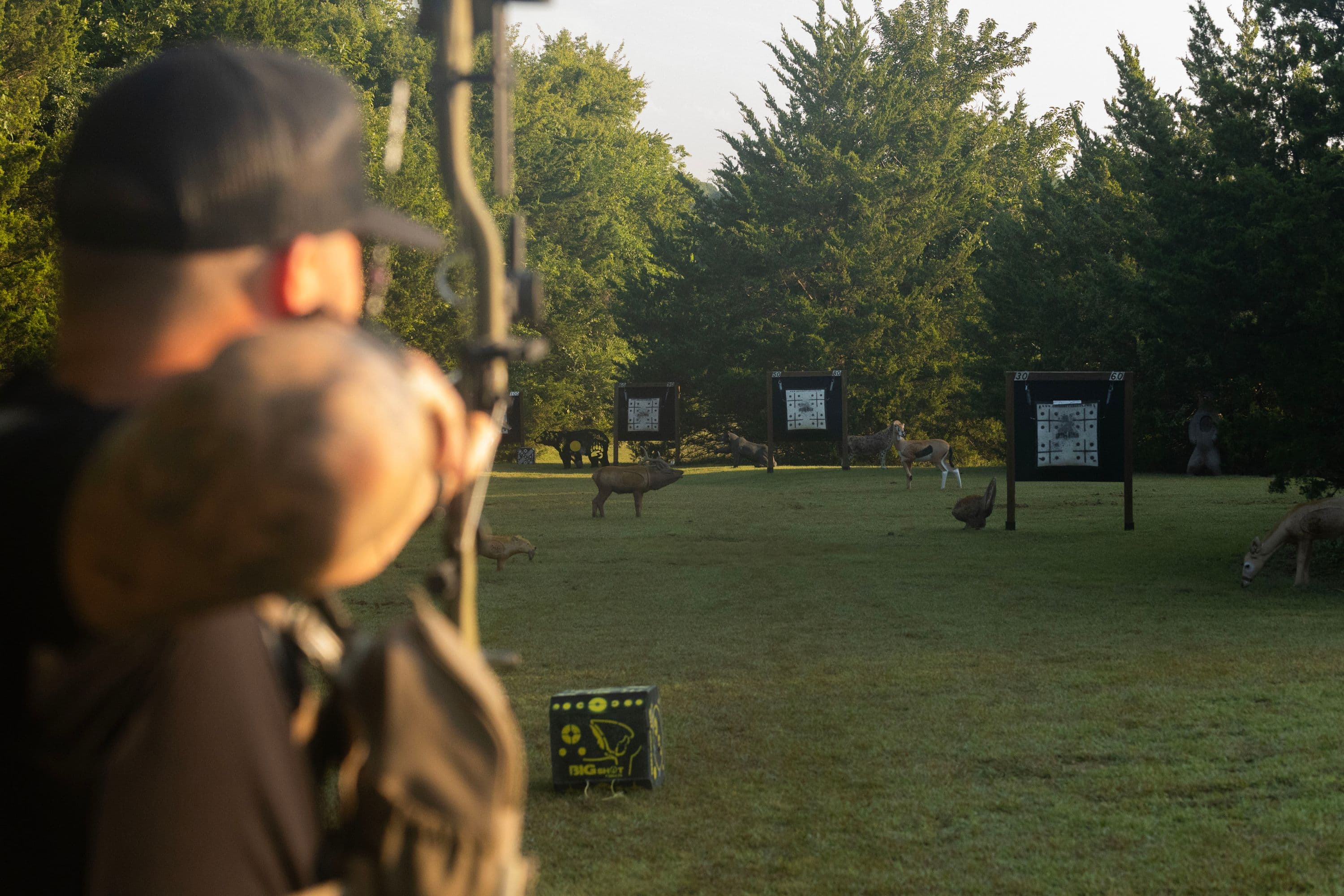 An archer at full draw on Bear River Archery's outdoor walk-back range, 3D animal targets in the distance
